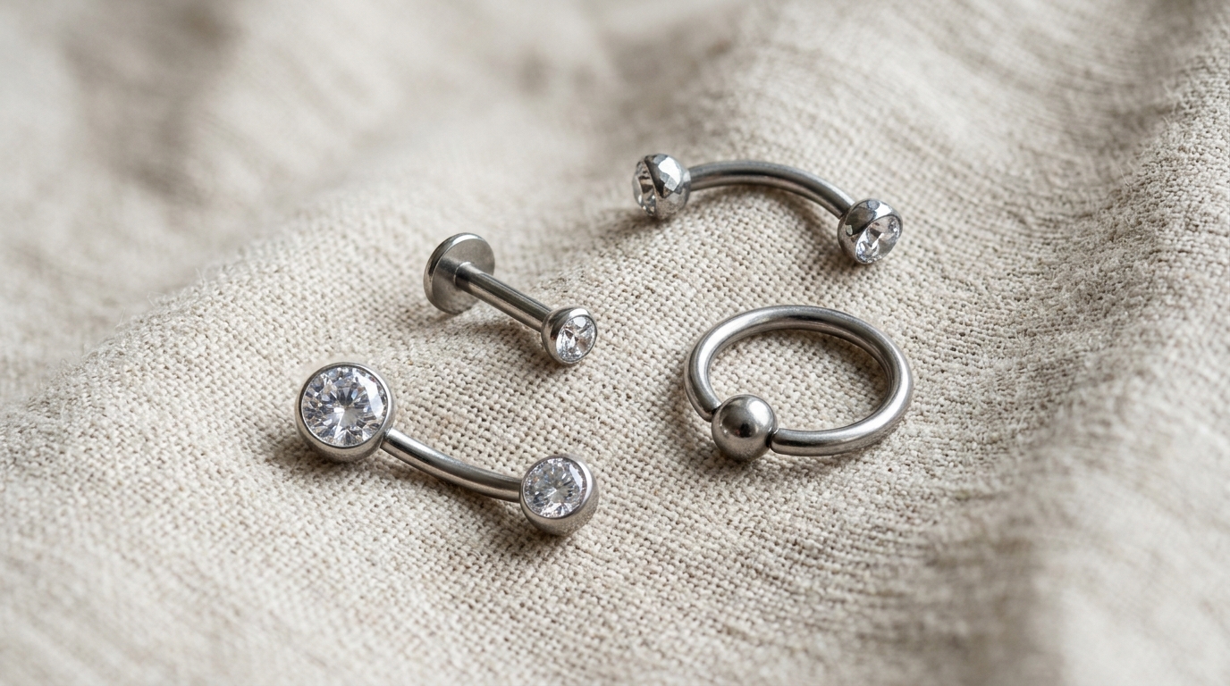 Collection of body jewelry styles: navel bananabell, eyebrow curved barbell, labret stud, and captive bead ring